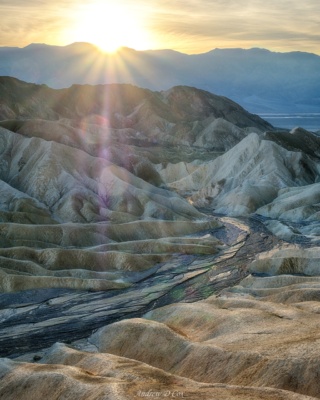 The last rays of sun stream over the distant Panamint Range and illuminate the sandy hills and dry riverbeds beneath Zabriskie Point. death valley zabriskie point sunset