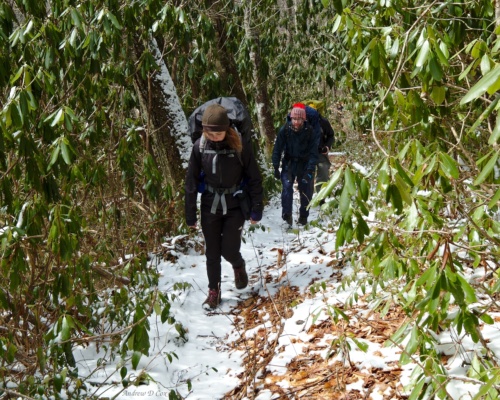 McKenzie and Ashley trek through the snow beneath rhododendrons smoky mountains winter backpacking