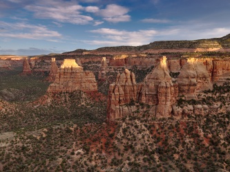 The sun breaks through the clouds momentarily, illuminating the tips of the spires and buttes before dipping below the horizon colorado national monument sunset