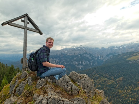 Robert poses with the summit marker and an epic expanse of mountains in the background alps kruezeck summit