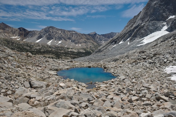The snowfield eventually runs out and we hop across talus to reach a small tarn sierra high route tarn