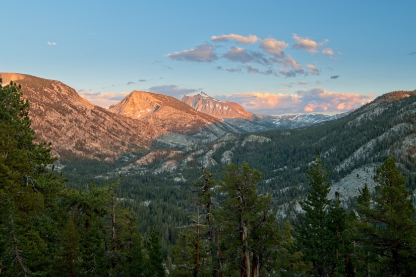 The red sunset light illuminates the triangular gables that given Seven Gables (the distant peak) its name. Undulating waves of granite carpeted in pines lie below the sunlit peaks. sierra nevada seven gables
