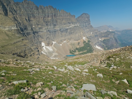 A bright teal tarn tucked into a small cirque below the sheer cliffs glacier national park tarn