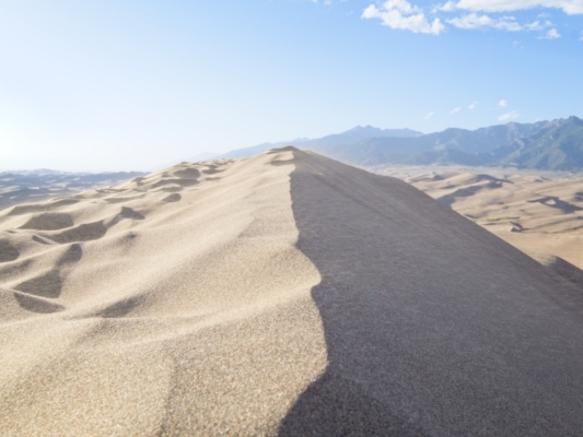 Sand blasts over the top of a dune