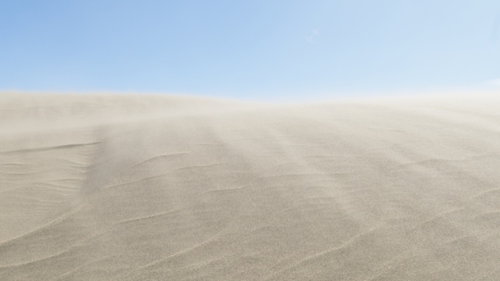 The fierce winds blow snow over the top of a dune