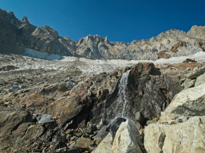 Glacial runoff cascades over the rocks. What's left of the glacier is covered in rocky debris middle palisade glacier