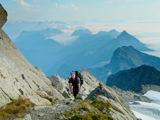 Craig J. on the trail up to the Three Fingers Lookout with clouds flowing over the ridge behind him cascades